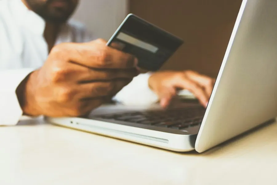 Person holding a payment card in one hand while typing on a laptop with the other